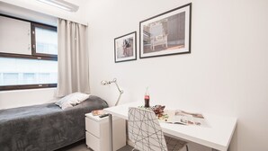 Un dormitorio pequeño y moderno con una cama individual, un escritorio y dos cuadros en la pared.