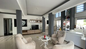 Un salon moderne avec un téléviseur à écran plat, une table basse en verre et deux fauteuils beiges.