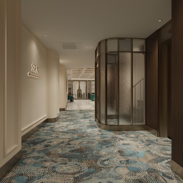 A hallway with a patterned carpet, a spa sign, and a glass elevator.