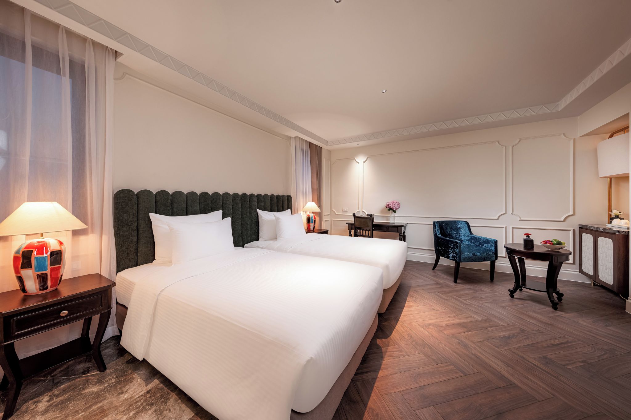 Een hotelkamer met twee bedden, een bureau, een stoel en een nachtkastje met een lamp.