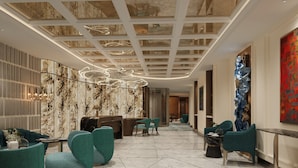A modern lobby with teal chairs, a reception desk, marble flooring, and a ceiling with a geometric pattern. - O'Gallery Signature Hotel & Spa (Hanoi)