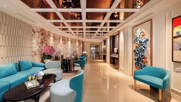 A modern hotel lobby with a marble wall, a seating area with blue sofas, a coffee table, and a decorative wall piece.
