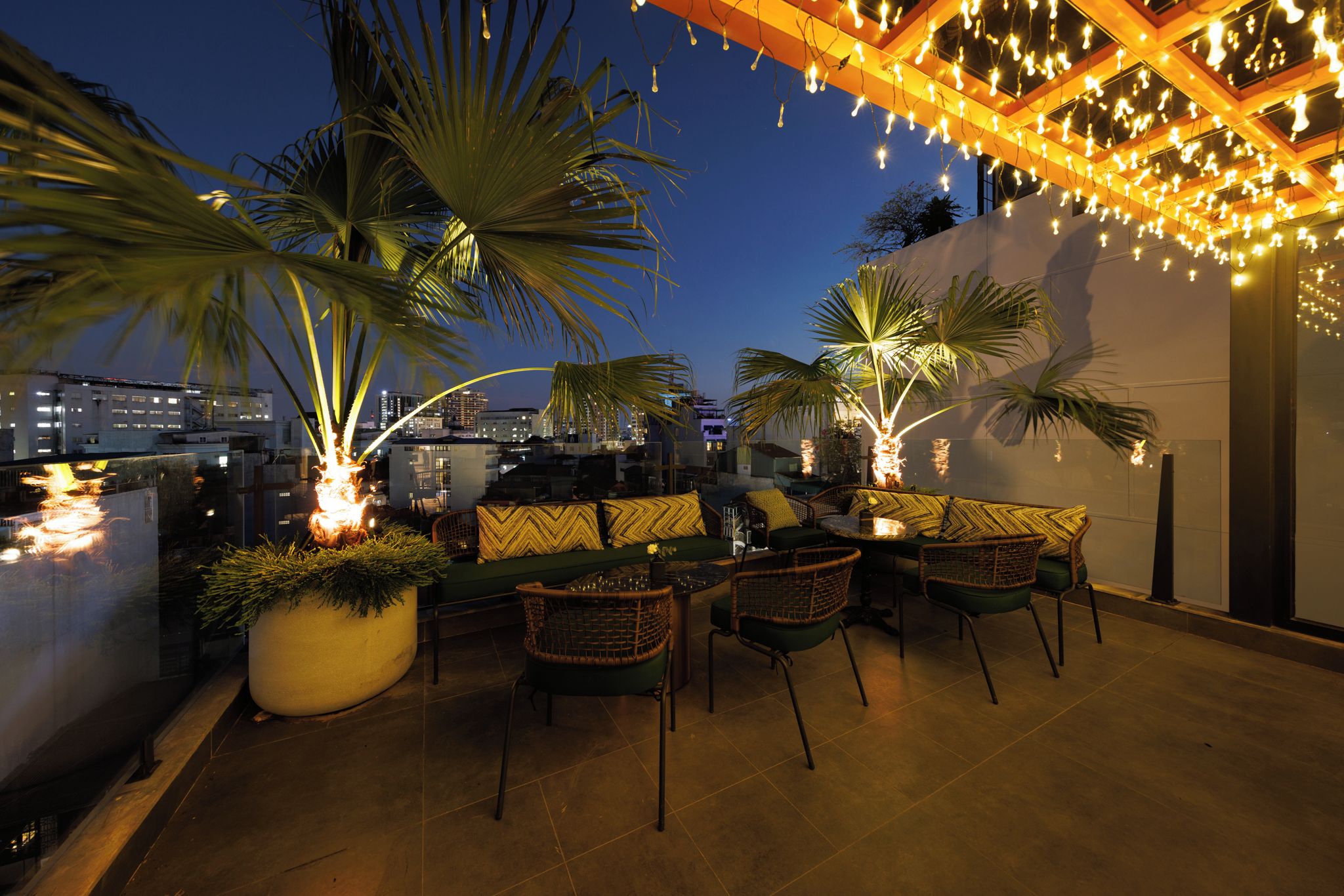 An outdoor seating area with wicker furniture, a large planter, and string lights.