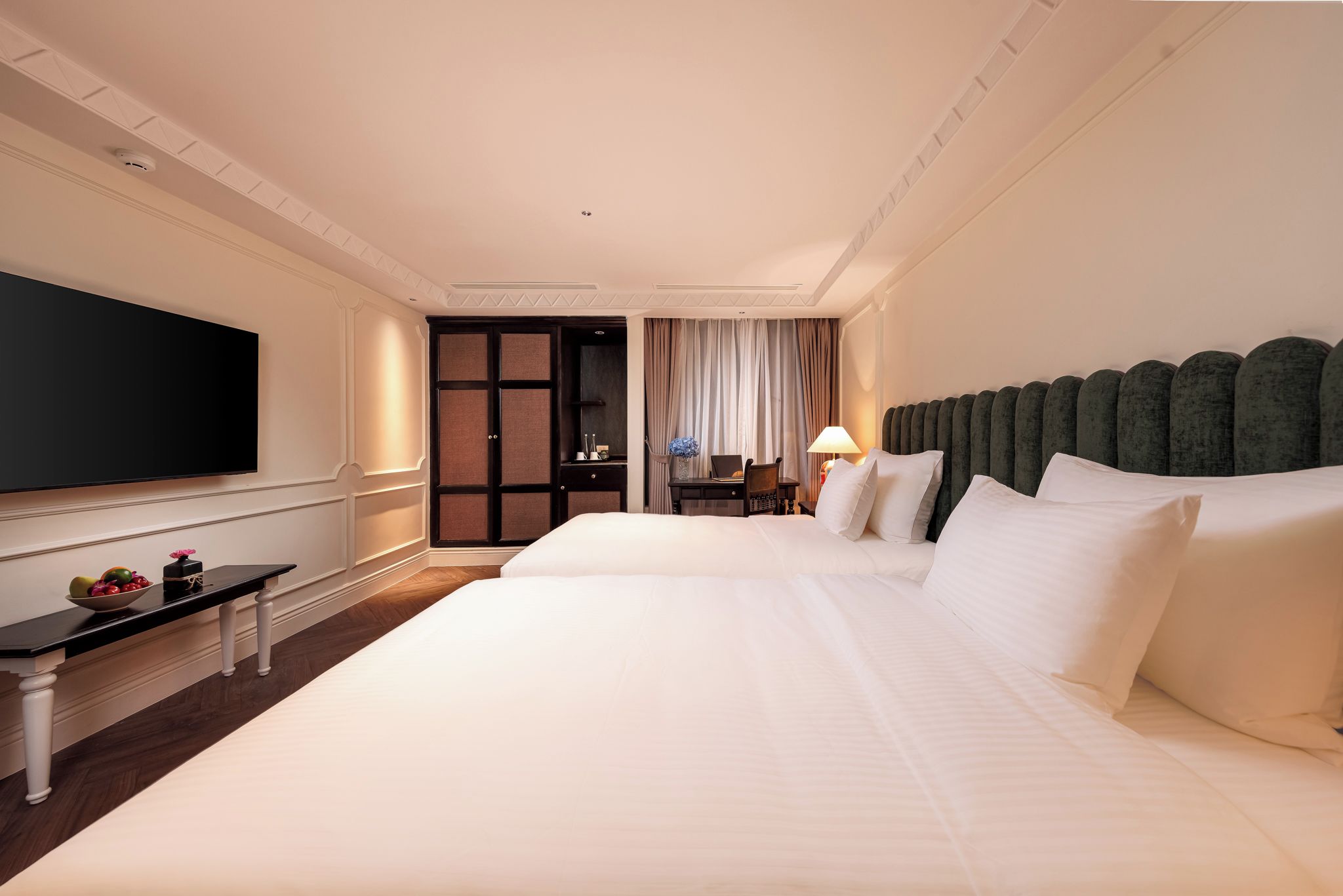 A hotel room with a large bed, a flat-screen TV, a desk with a laptop, and a window with curtains.