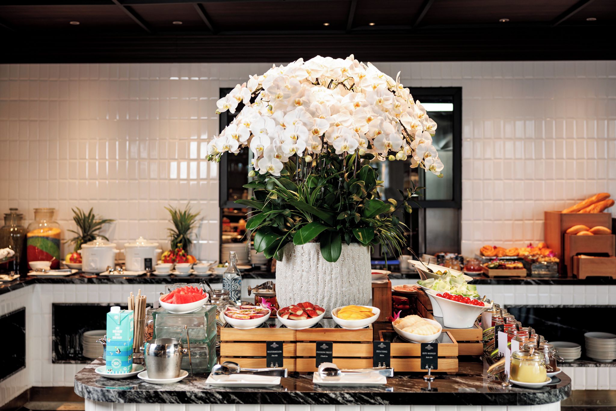 A buffet setup with a variety of food items and a centerpiece of white orchids.