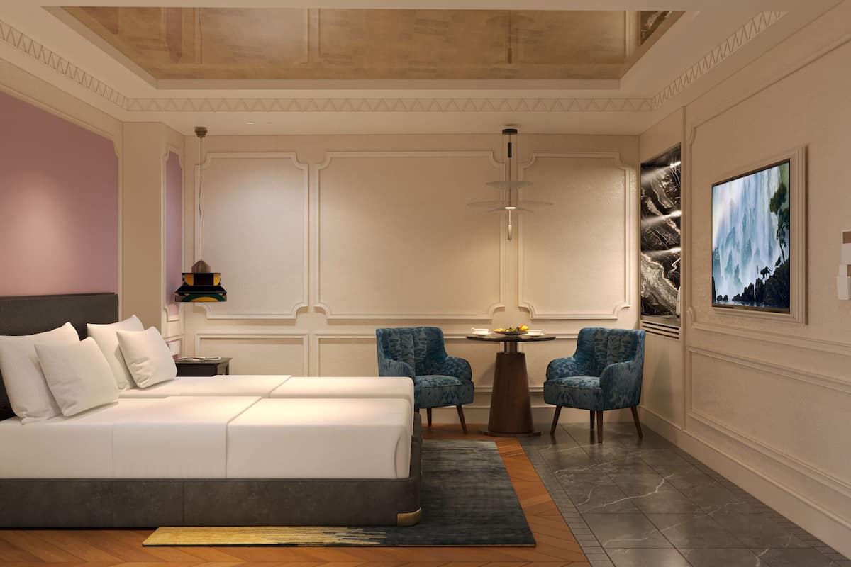 A modern hotel room with a large bed, two armchairs, a small table, and a TV.