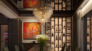 A dining area with a long table, chairs, a chandelier, and a wall with shelves of bottles. - O'Gallery Signature Hotel & Spa (Hanoi)