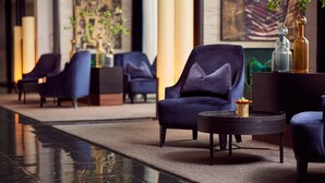 Eine moderne Lobby mit dunkelblauen Sesseln, einem runden schwarzen Tisch mit einer Vase und einem polierten Boden, der den Raum spiegelt.