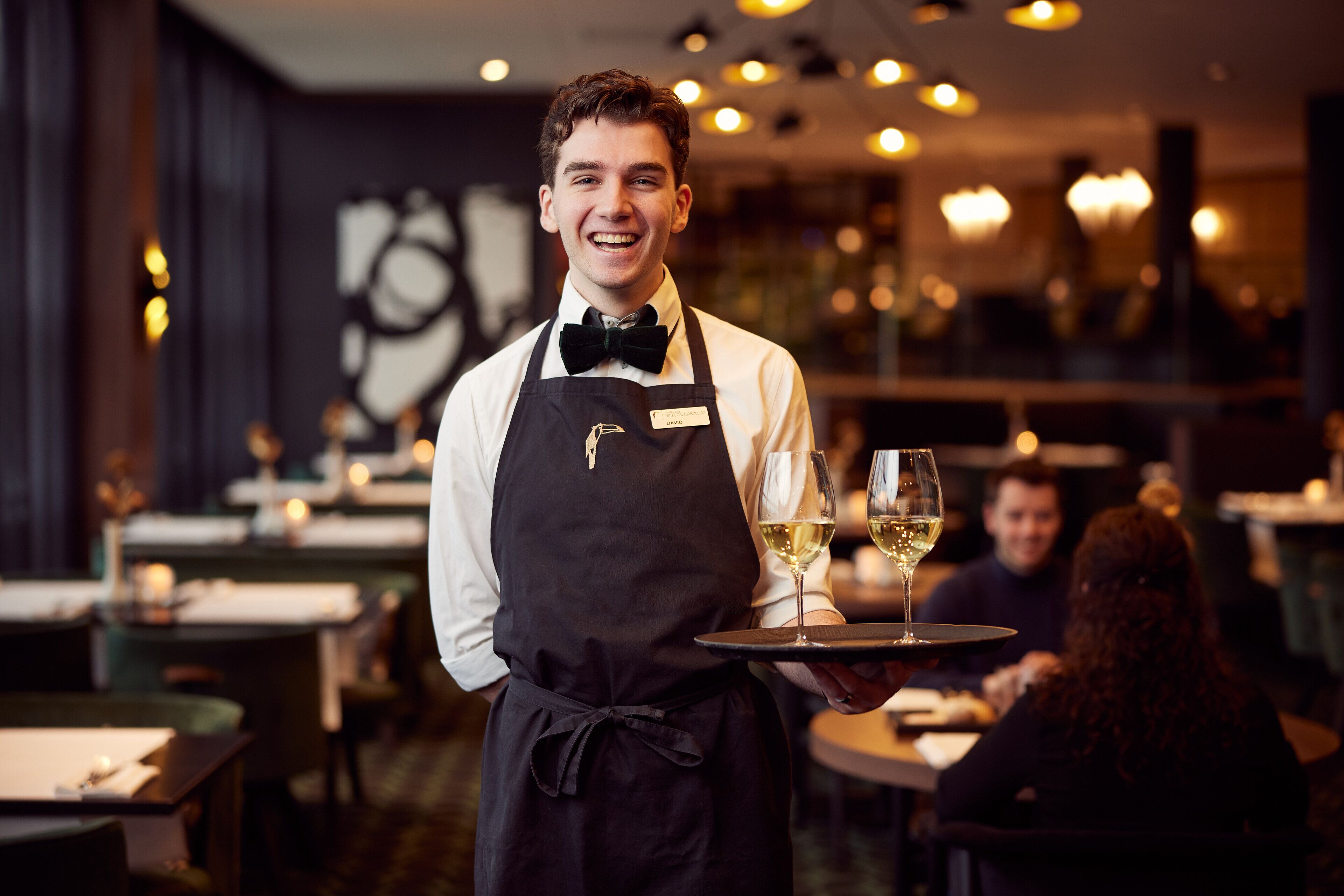 A waiter in a restaurant holding a tray with two glasses of wine.