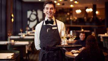 A waiter in a restaurant holding a tray with two glasses of wine.