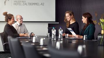 A conference room with a projector screen displaying the hotel name, a table with water bottles, and a laptop.