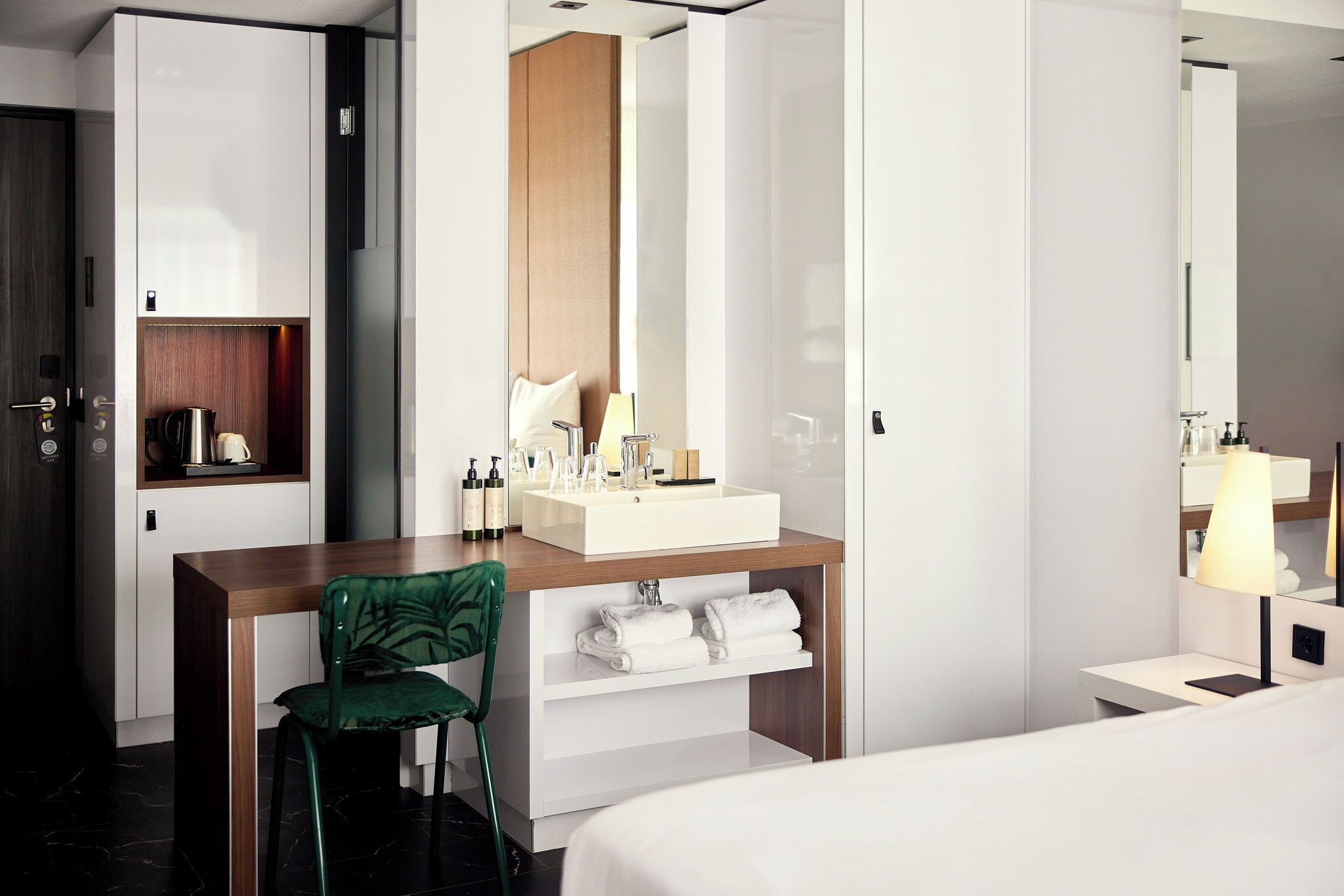 Une chambre d’hôtel moderne avec un bureau en bois, une chaise verte, un lavabo blanc et un lit.