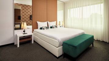 Habitación de hotel con una cama grande, un banco, una mesita de noche, un espejo y una ventana con cortinas.