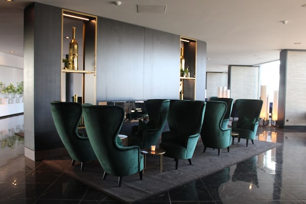 A modern lobby with green upholstered chairs, a marble floor, and a central table with a candle.