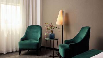 Een hotelkamer met twee groene fauteuils, een tafeltje met een bloevas en een lamp.