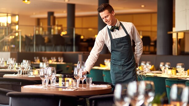 Ein Restaurant mit gedeckten Tischen, einem Kellner in Uniform und modernem Interieur.