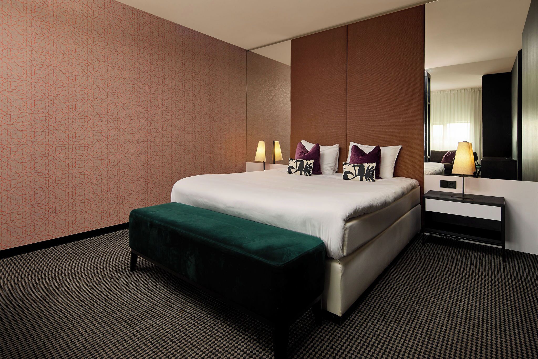 Een hotelkamer met een bed, bedlampen, een nachtkastje, een spiegel en een groene bank.