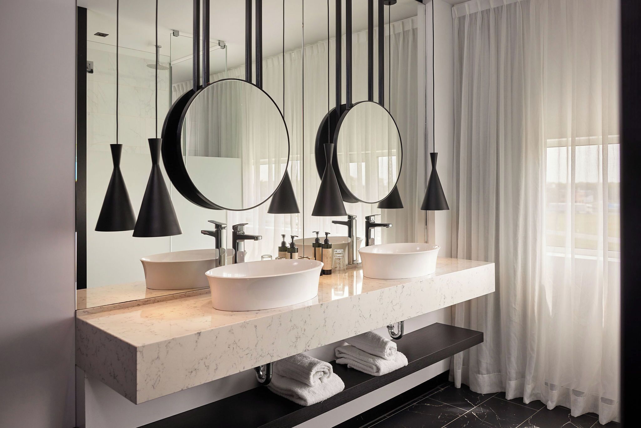 A modern bathroom with two sinks, large mirrors, and pendant lights.
