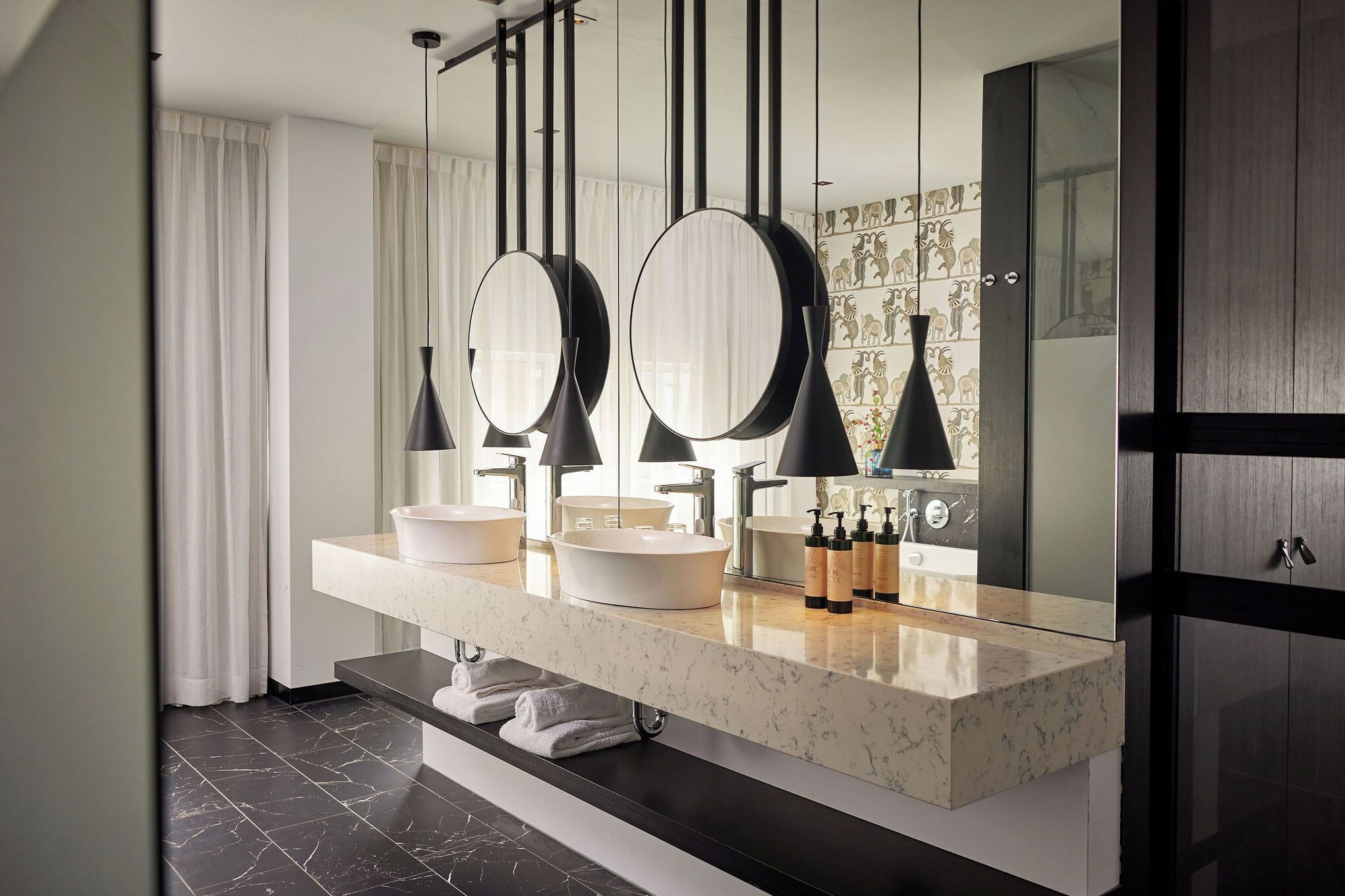 A modern bathroom with a double vanity, two round mirrors, black pendant lights, and a marble countertop.