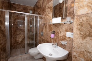 Een moderne badkamer met een glazen douchecabine, een witte wastafel en marmeren wanden.