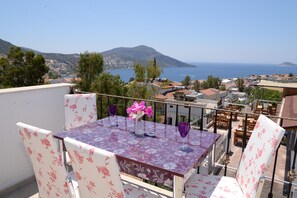 Een balkon met een tafel en stoelen, met uitzicht op een kustplaatsje en een berg.