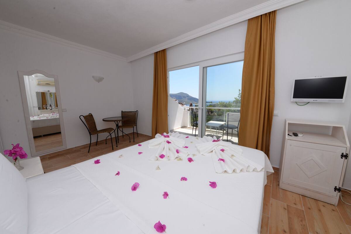 A hotel room with a bed, a desk, a chair, a television, and a balcony with a view.