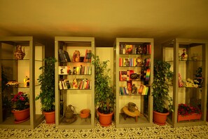 A room with three glass-fronted bookcases filled with books and decorative items, flanked by potted plants. - Neruda Hotel (Kas)