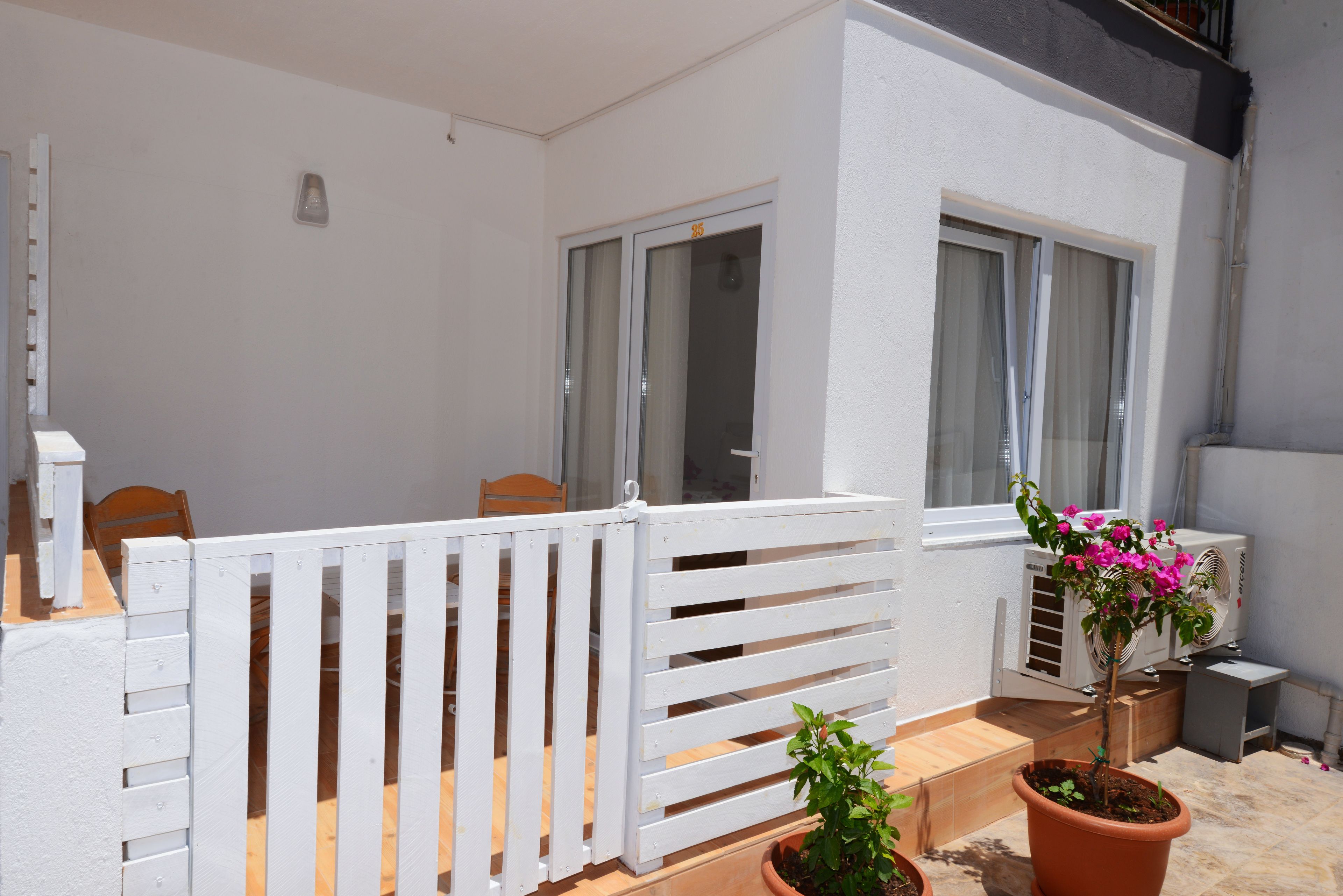 A balcony with a white railing, a potted plant, and an air conditioning unit.