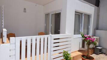 A balcony with a white railing, a potted plant, and an air conditioning unit.