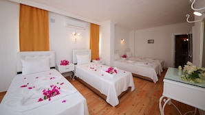 A hotel room with three single beds, each with a white bedspread and pink flowers. There are white nightstands with lamps, a wooden floor, and a glass table with a vase of flowers. - Neruda Hotel (Kas)