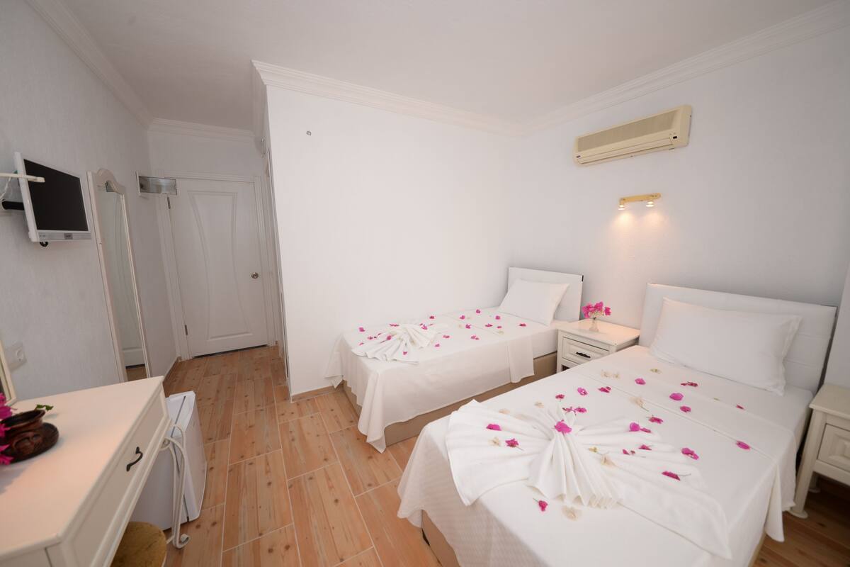 A hotel room with two beds, a desk, a TV, and a wall-mounted air conditioner.
