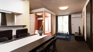 Habitación de hotel con una mesa de comedor, sillas, un florero con flores, un televisor y un equipo de aire acondicionado.