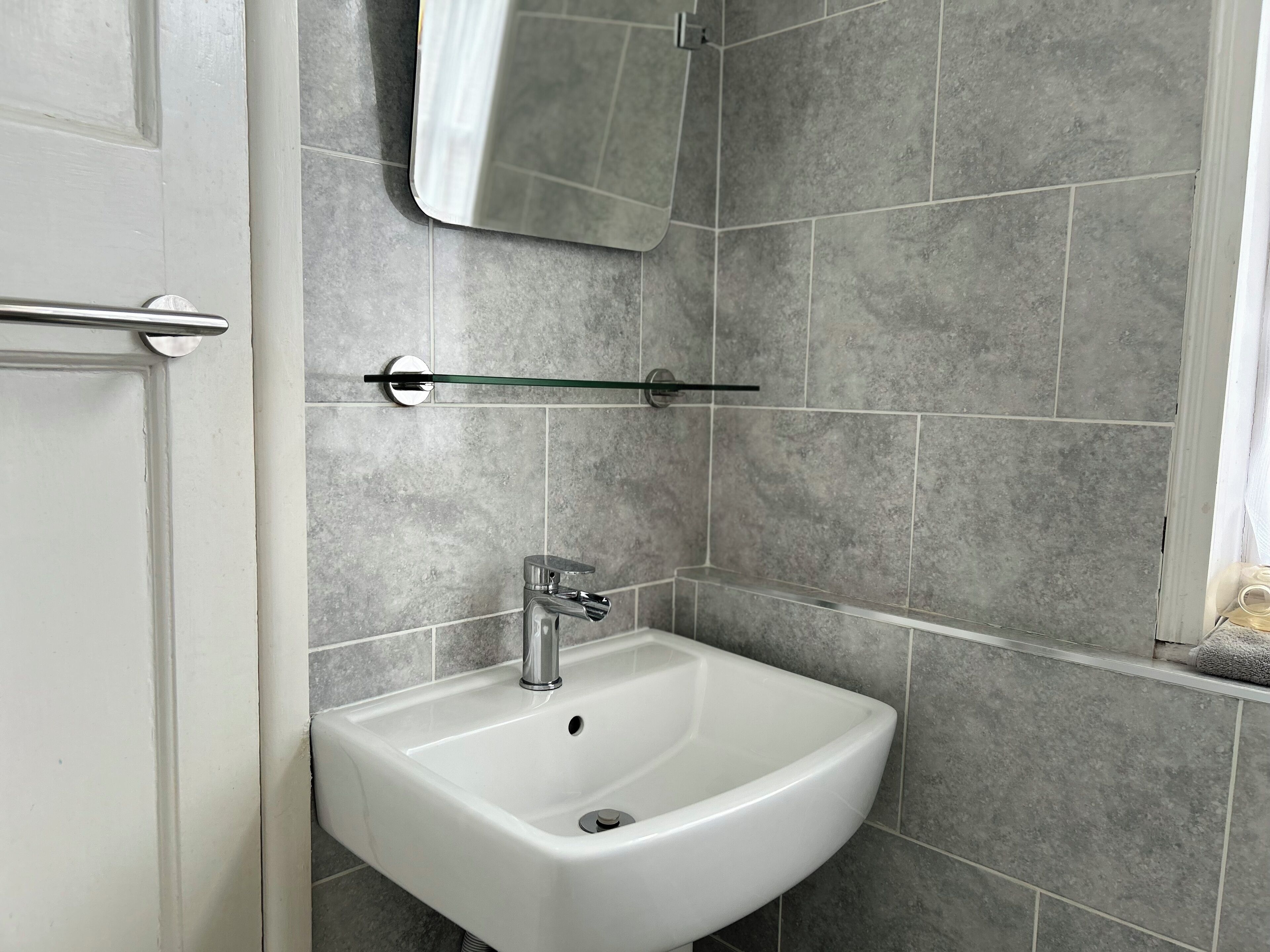A bathroom with a white sink, a mirror, and grey tiled walls.