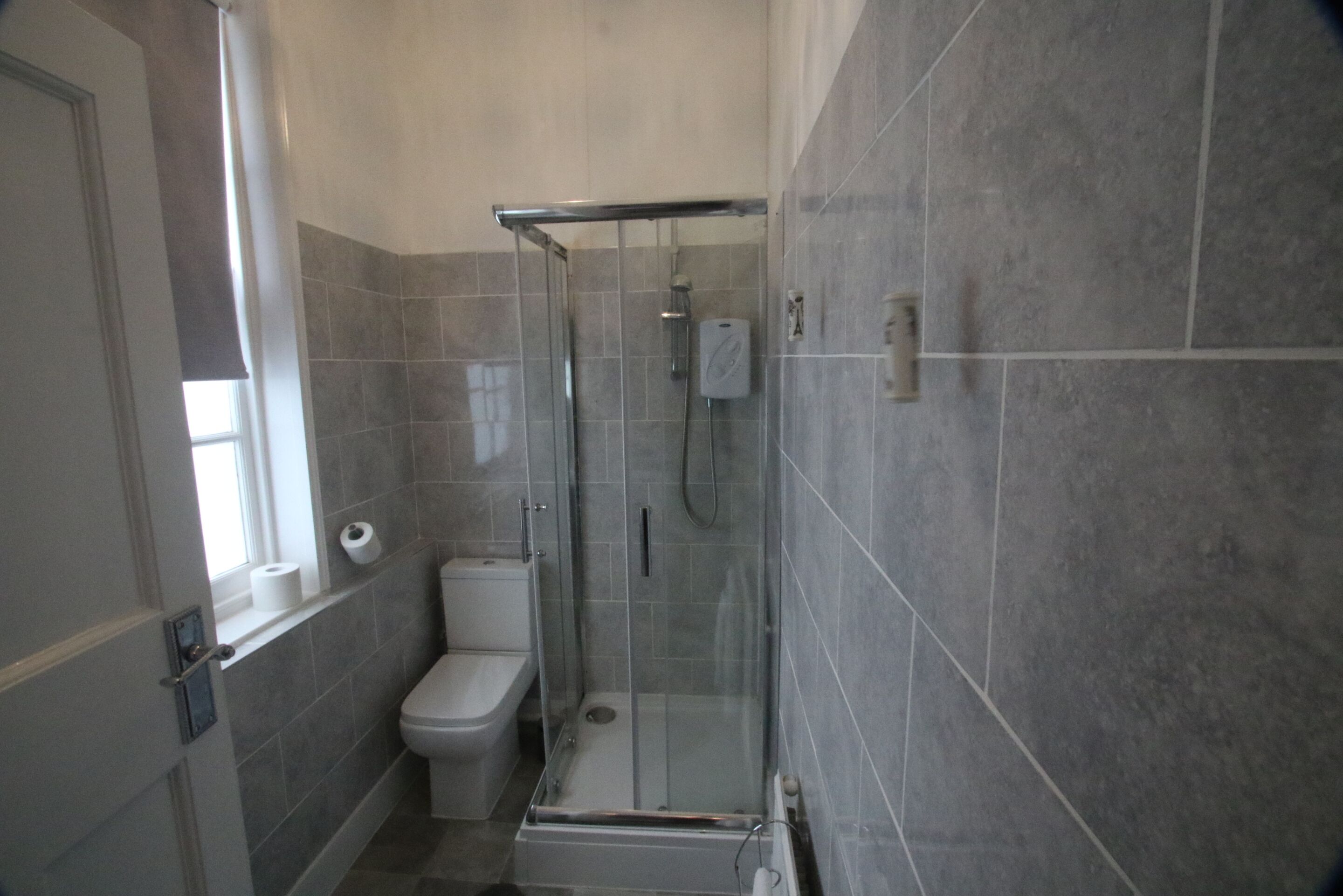 Een moderne badkamer met een glazen douchecabine, een toilet en een raam met uitzicht.