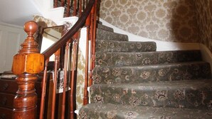 Escadaria com balaústres de madeira ornamentados e degraus cobertos por um tapete estampado.