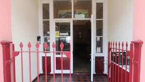 Entrada de hotel com chão quadriculado em vermelho e branco, porta de vidro e portão de metal vermelho.