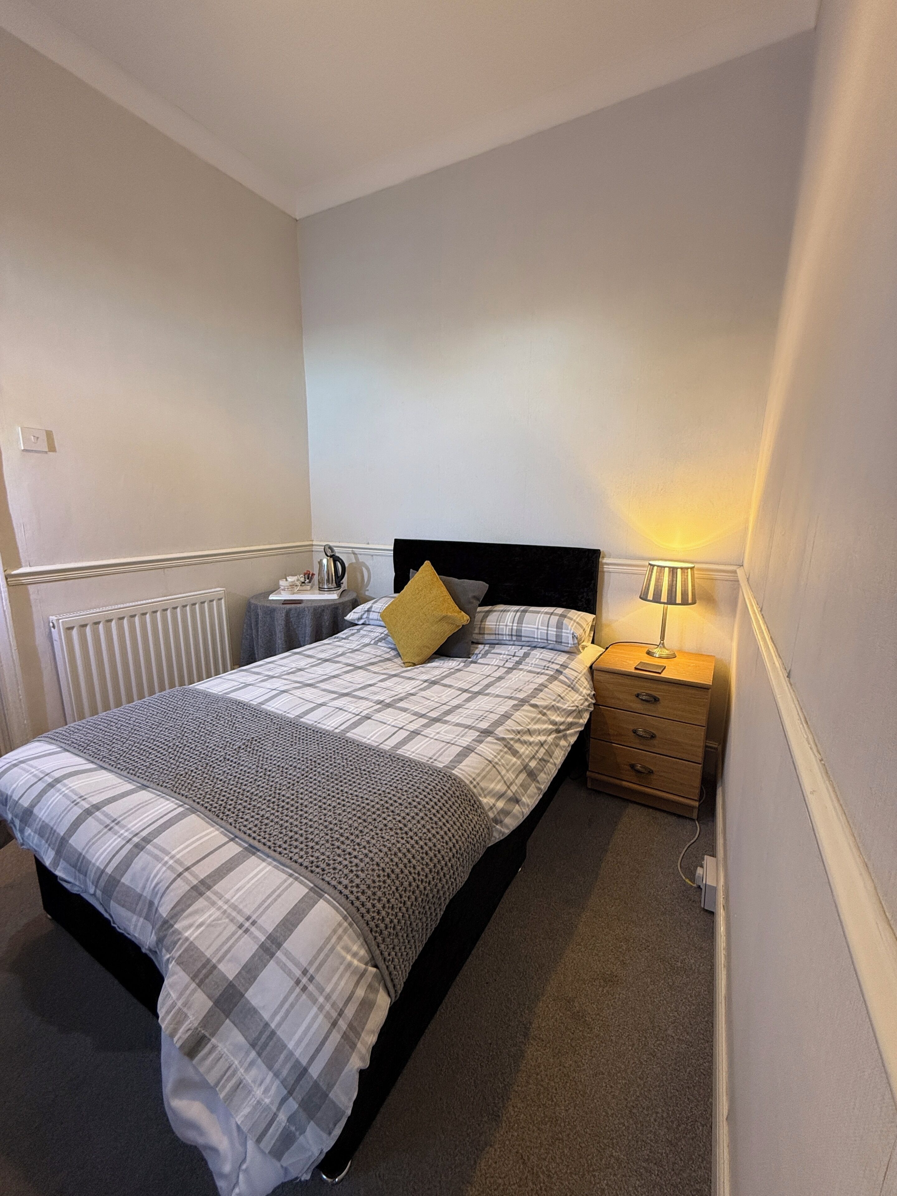 A bedroom with a bed, bedside table, lamp, and radiator.