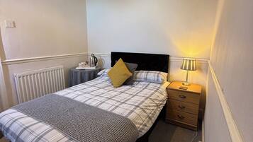 A bedroom with a bed, bedside table, lamp, and radiator.