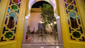 Un patio interior con suelo de baldosas, una fuente central y un árbol.