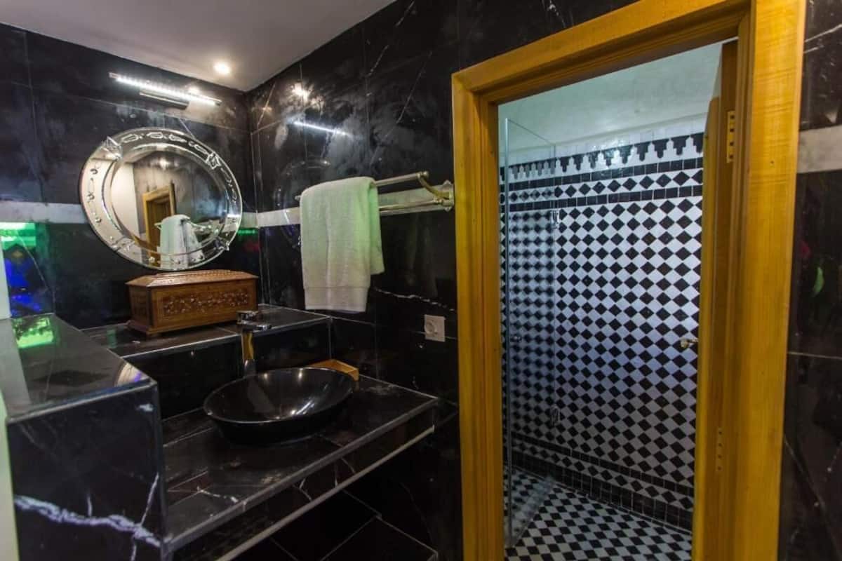A bathroom with a black and white checkered shower wall, a round mirror, and a sink with a bowl.