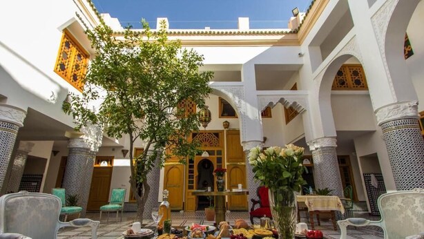 Un patio tradicional marroquí con una mesa lista para comer, sillas y un árbol decorativo.