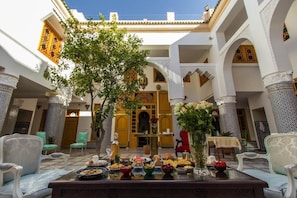 A traditional Moroccan courtyard with a dining setup, including a table with food, chairs, and a decorative tree. - Riad Amor (Fes)