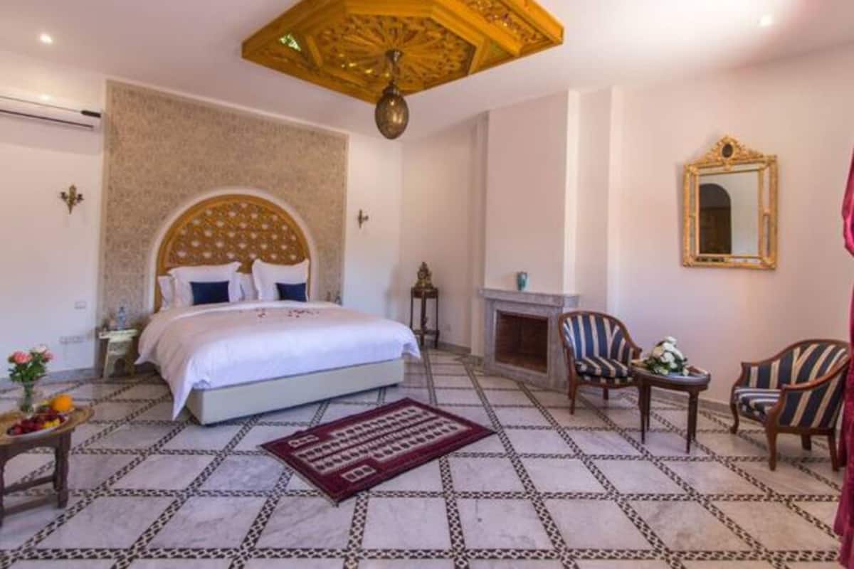 A bedroom with a large bed, a fireplace, a mirror, and a patterned floor.