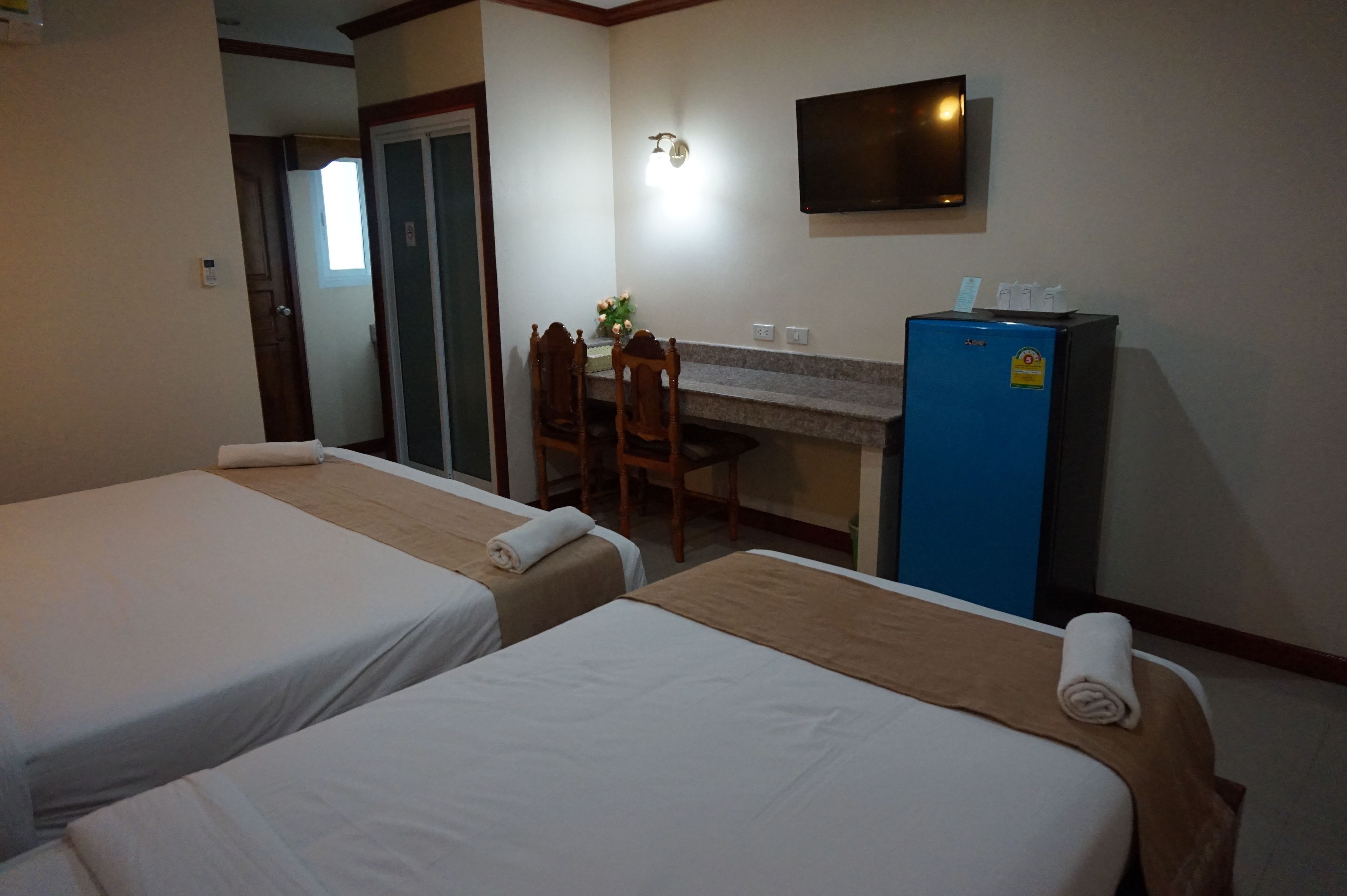 Habitación de hotel con dos camas, un escritorio pequeño con silla, un televisor montado en la pared y un refrigerador.