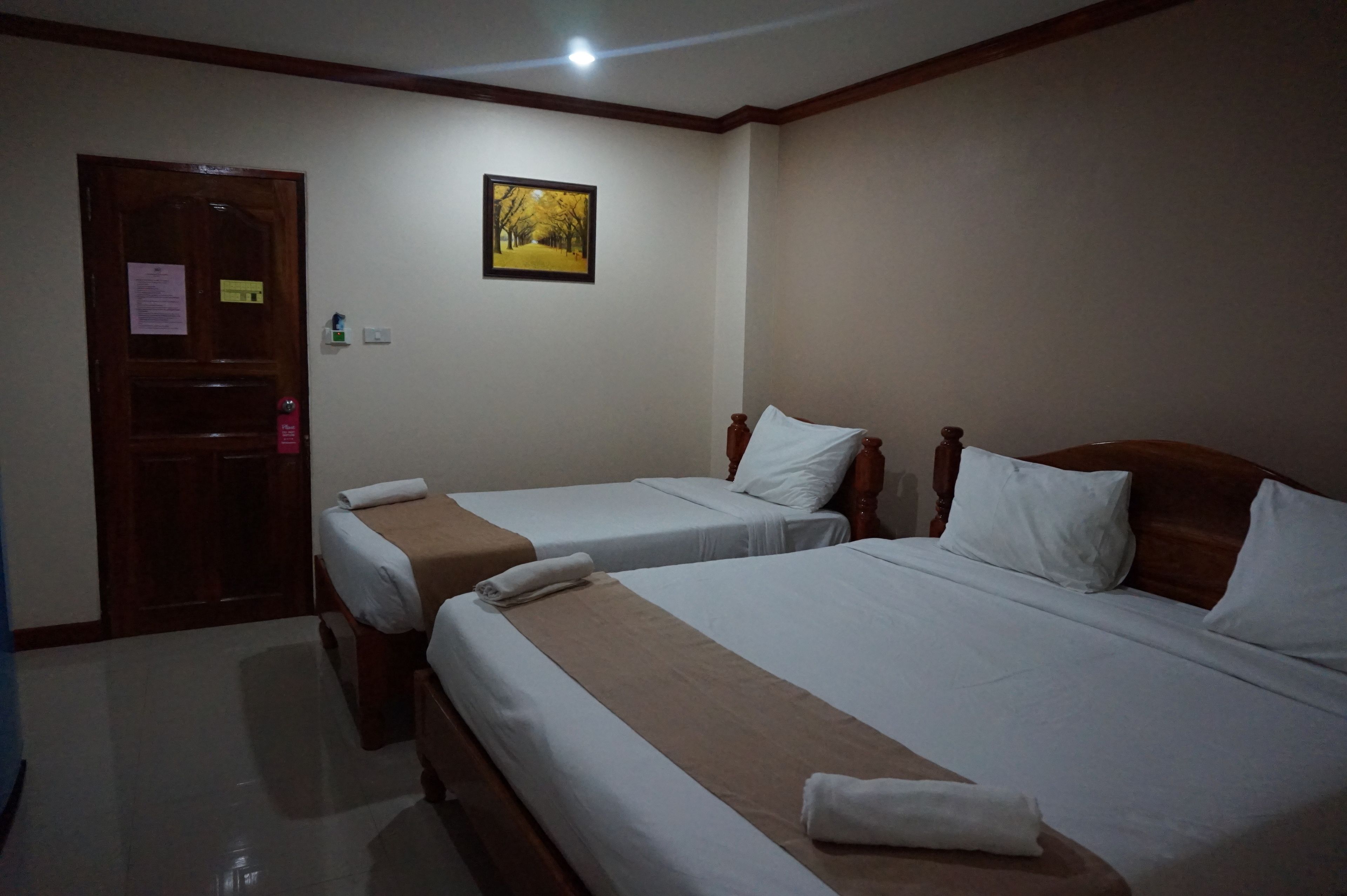 A hotel room with two single beds, a wooden door, a framed picture on the wall, and a small window.