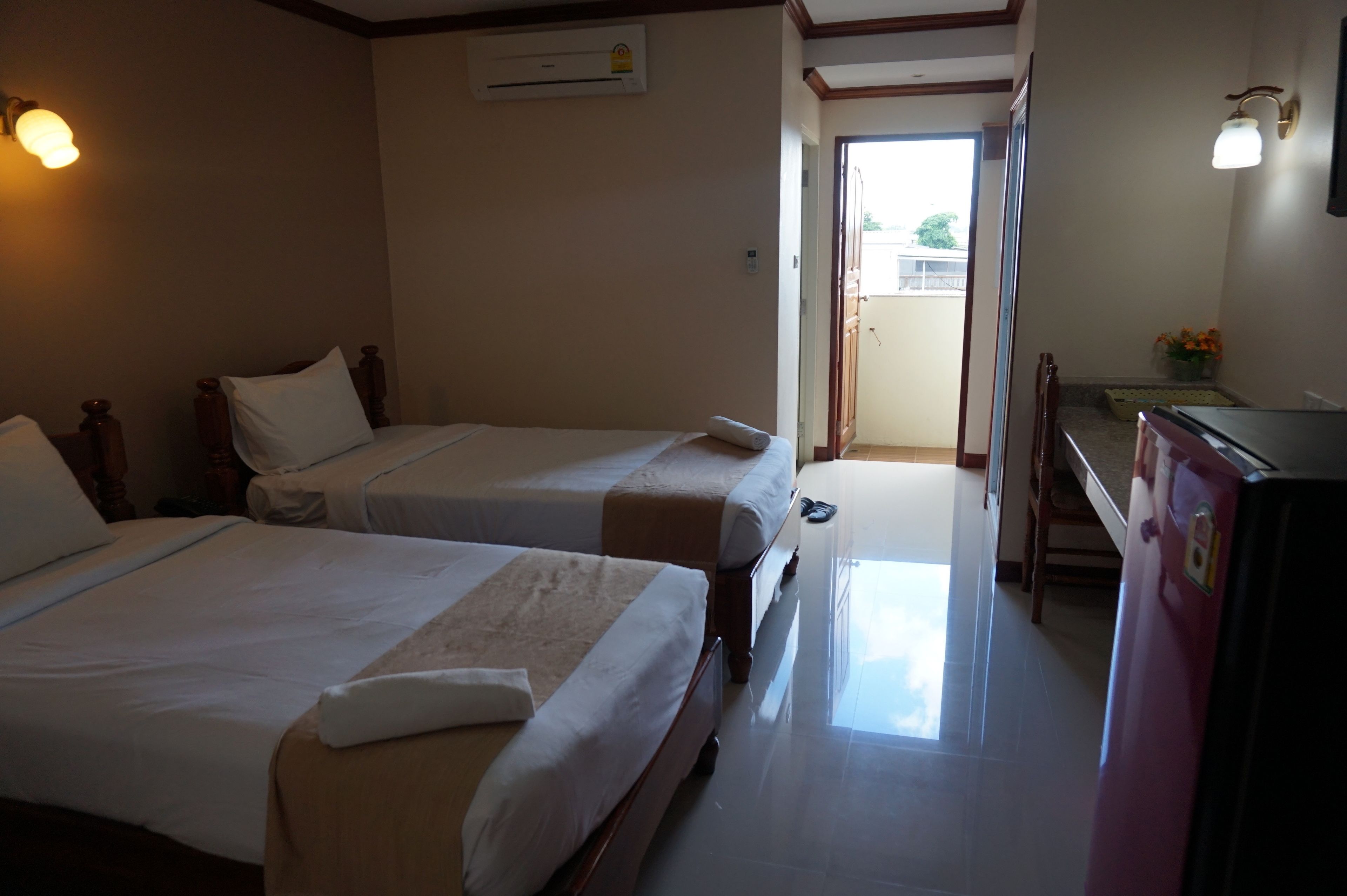 A hotel room with two beds, a refrigerator, a small table, and a door leading to a balcony.
