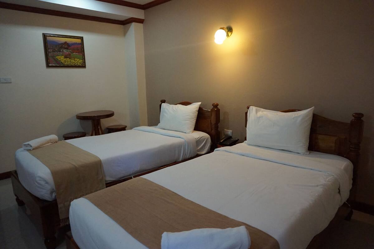 Ein Hotelzimmer mit zwei Einzelbetten, einem kleinen Tisch, einer Wandleuchte und einem gerahmten Bild an der Wand.