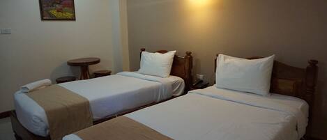 A hotel room with two single beds, a small table, a wall-mounted light, and a framed picture on the wall.