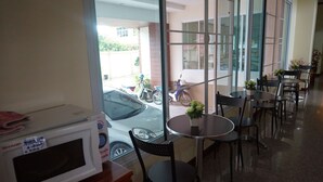 A restaurant with a view of parked cars and a motorcycle outside. There are tables and chairs inside. - NP Residence (Nakhon Phanom)