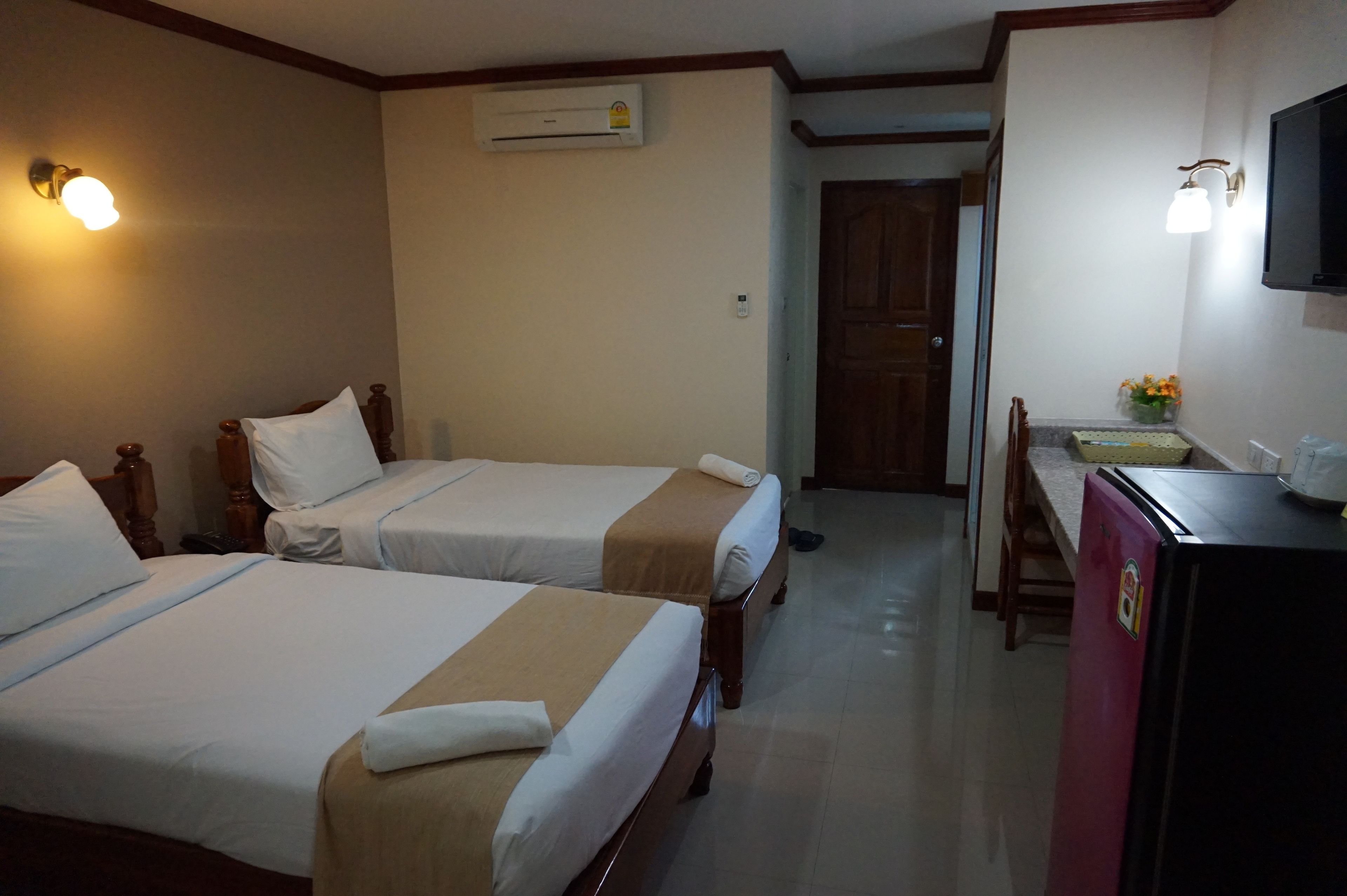 Habitación de hotel con dos camas, un escritorio con silla, un refrigerador y un equipo de aire acondicionado.